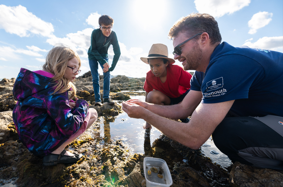 A Plymouth Sound National Marine Park Coastal Ranger showing a group of children a cushion star found in a rockpool at Mount Batten Beach.