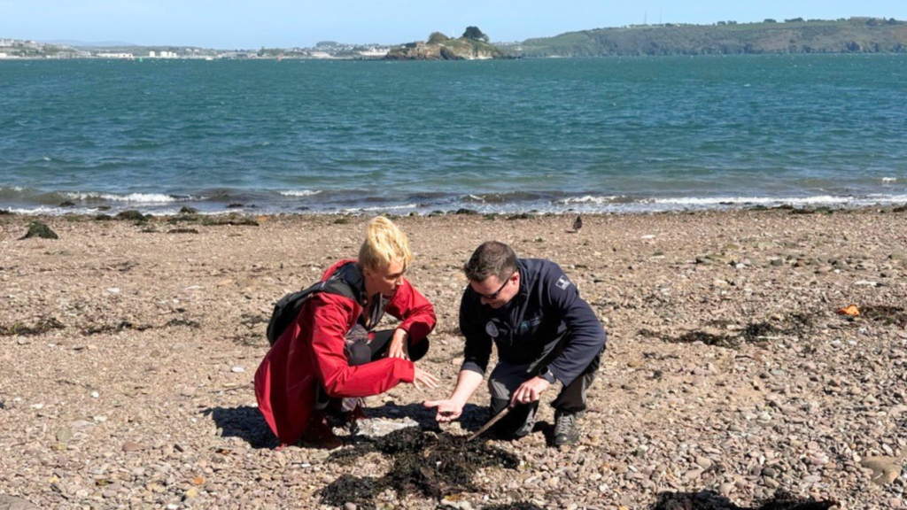 Zanna, wearing a red coat sits with Head Ranger Sam looking at rock pool.
